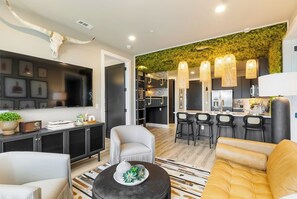 A modern living room with a TV, sofa, chairs, and a dining area with bar stools. - Bourbon & Broadway - Luxury Living 1.3 miles to Broadway, Brand New, 6 Beds! (Nashville)