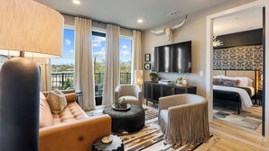 Ein modernes Hotelzimmer mit Sofa, Sessel, Fernseher und einem Balkon mit Blick.