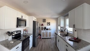 A kitchen with white cabinets, a microwave, stove, refrigerator, and a sink. - FIFA Neat Nest (Raytown)