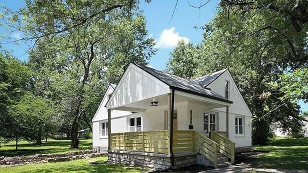A white house with a porch, a stone foundation, and a staircase leading to the entrance. - FIFA Neat Nest (Raytown)