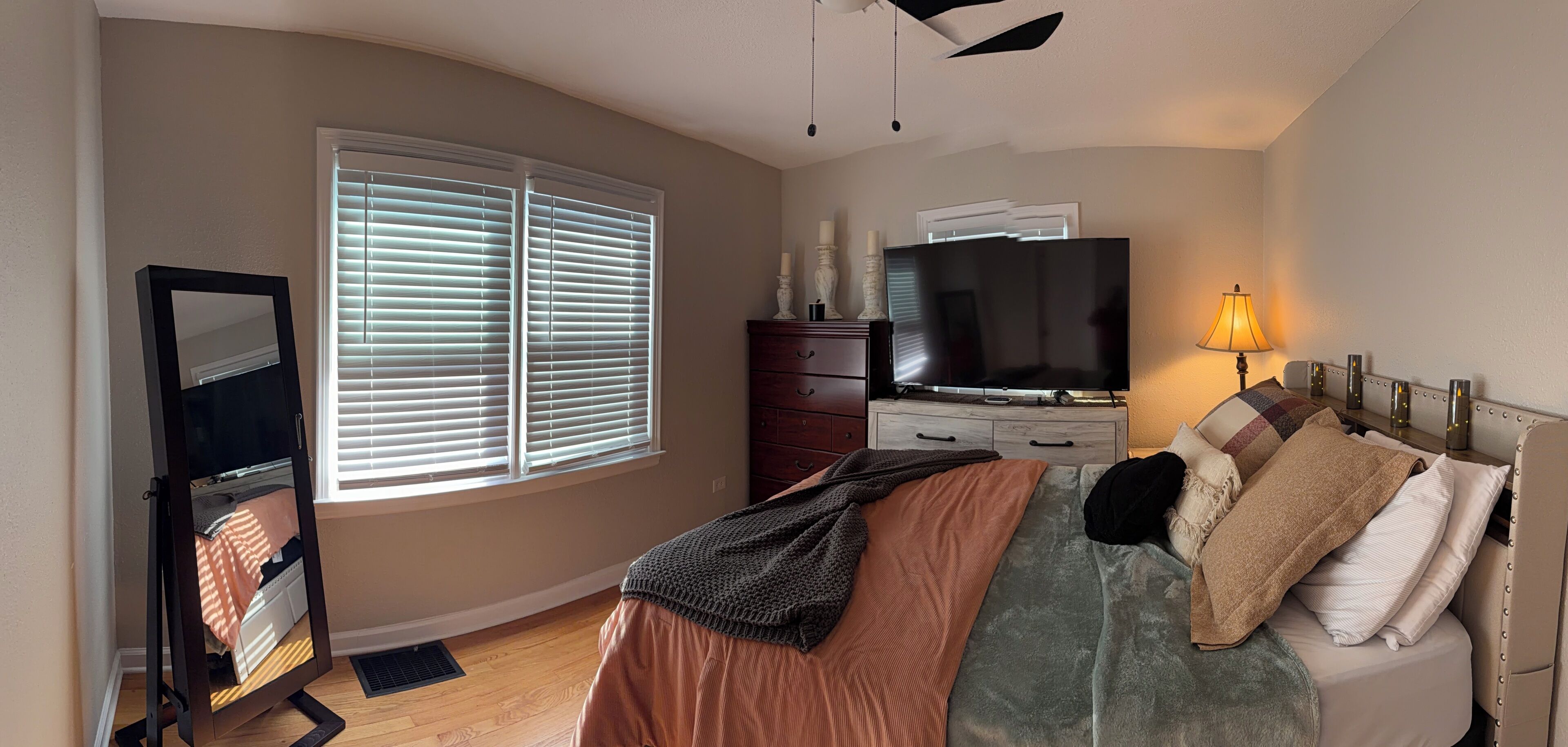 A bedroom with a bed, dresser, TV, and window with blinds.