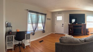 A living room with a fireplace, a sofa, a TV, and a desk with a chair. - FIFA Neat Nest (Raytown)