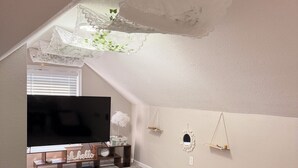 An attic room with a TV, green sofas, a wooden coffee table, and a hanging light fixture. - FIFA Neat Nest (Raytown)