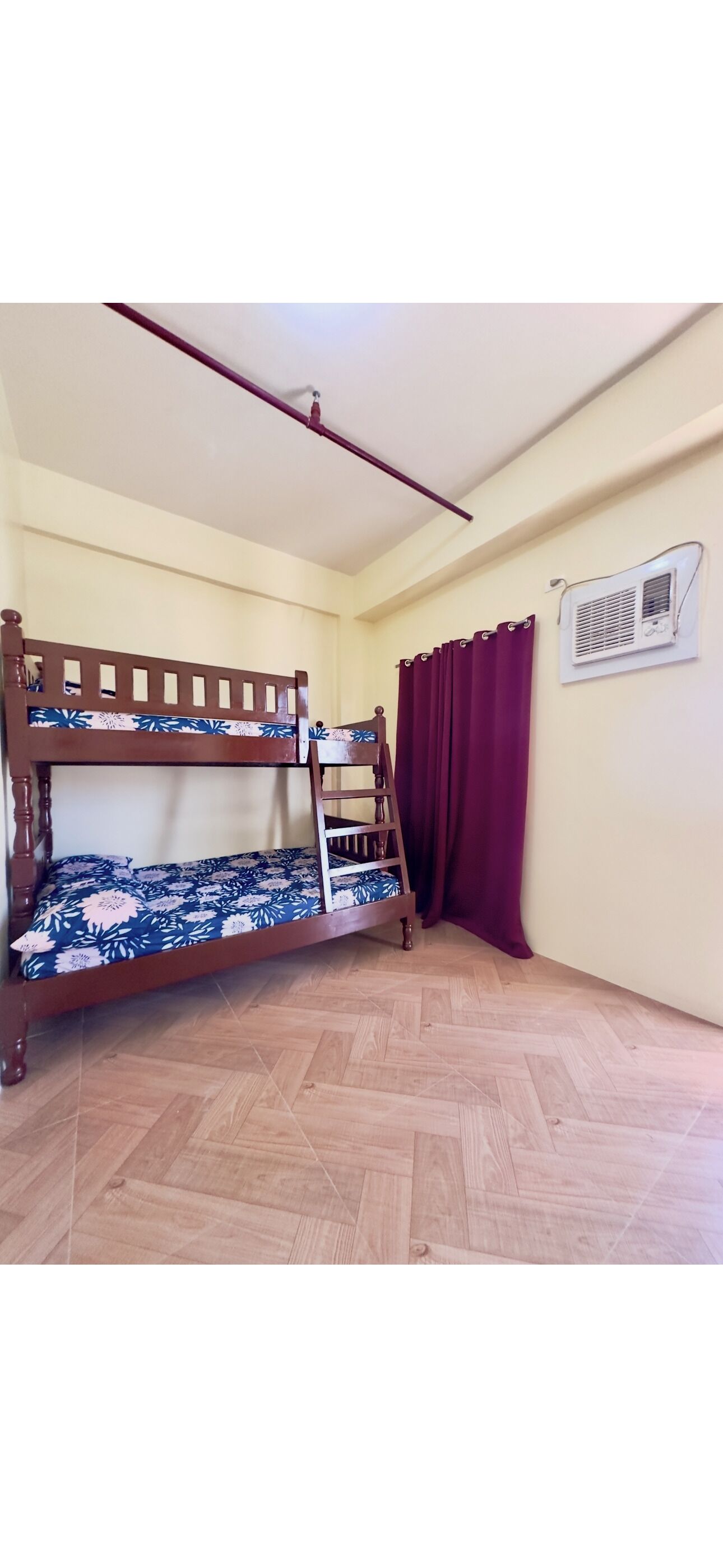 Una cama litera con colchón estampado de flores, una escalera y un aire acondicionado fijado a la pared.