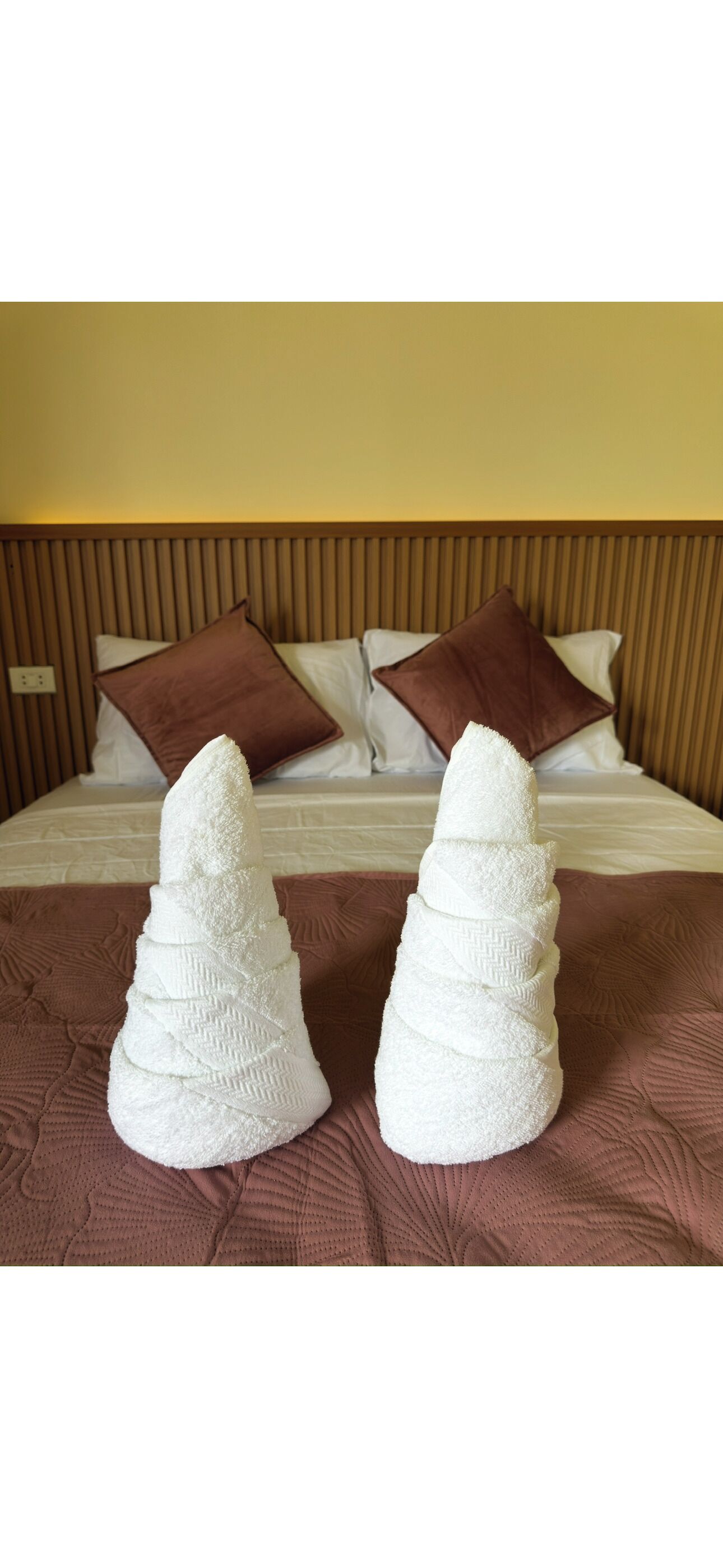 Un lit avec une tête de lit en bois, deux oreillers marron et deux serviettes blanches disposées sur le lit.