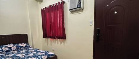 A bedroom with a bed, a window with curtains, a door, and a table with a box.