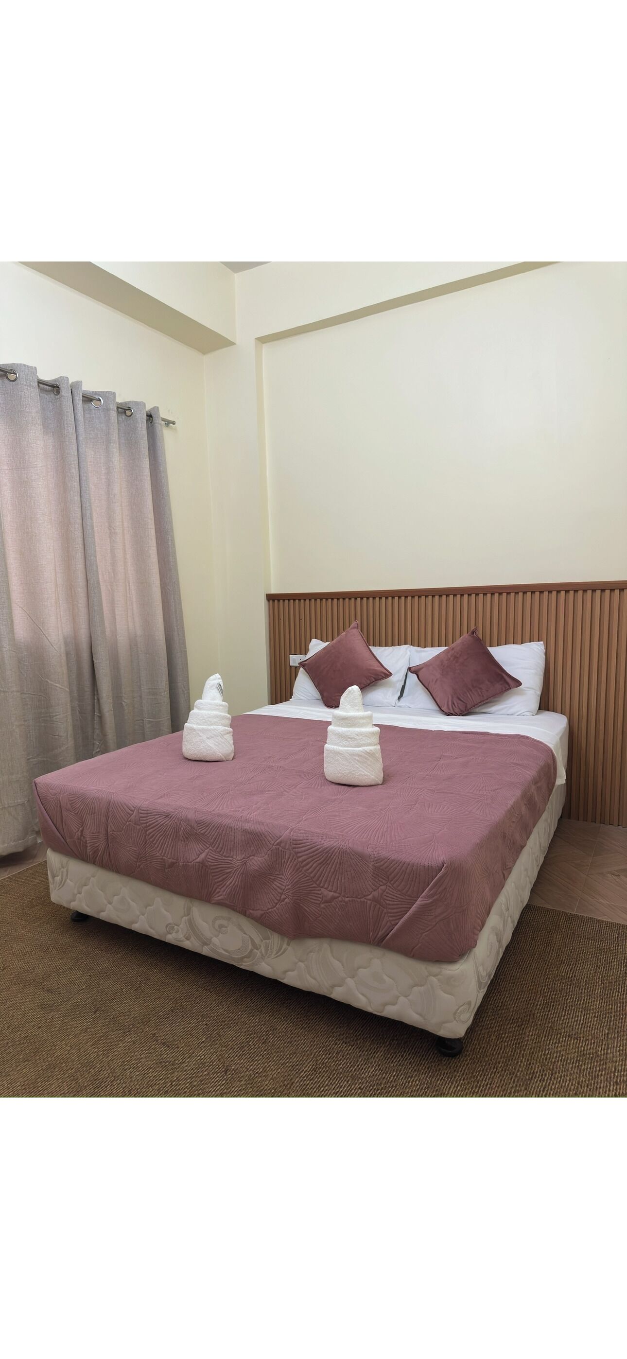 A neatly made bed with a headboard, a pair of towels, and a curtain.