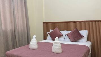 A neatly made bed with a headboard, a pair of towels, and a curtain.