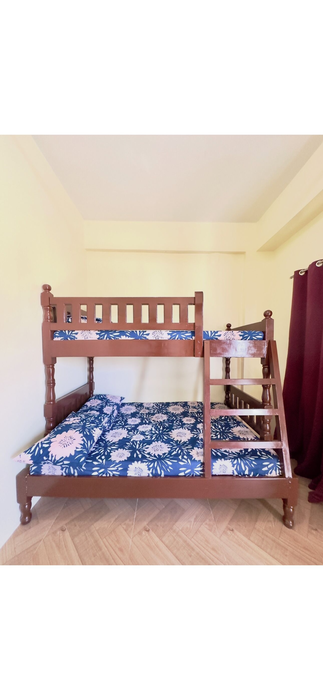 A bunk bed with a floral-patterned mattress in a room with wooden flooring and a plain wall.