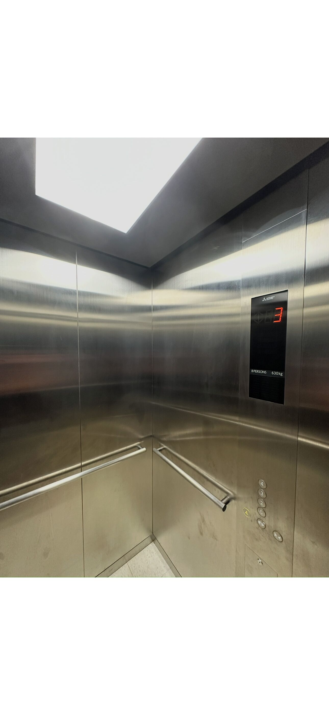 A modern elevator with a digital display, metallic walls, and a clear ceiling.