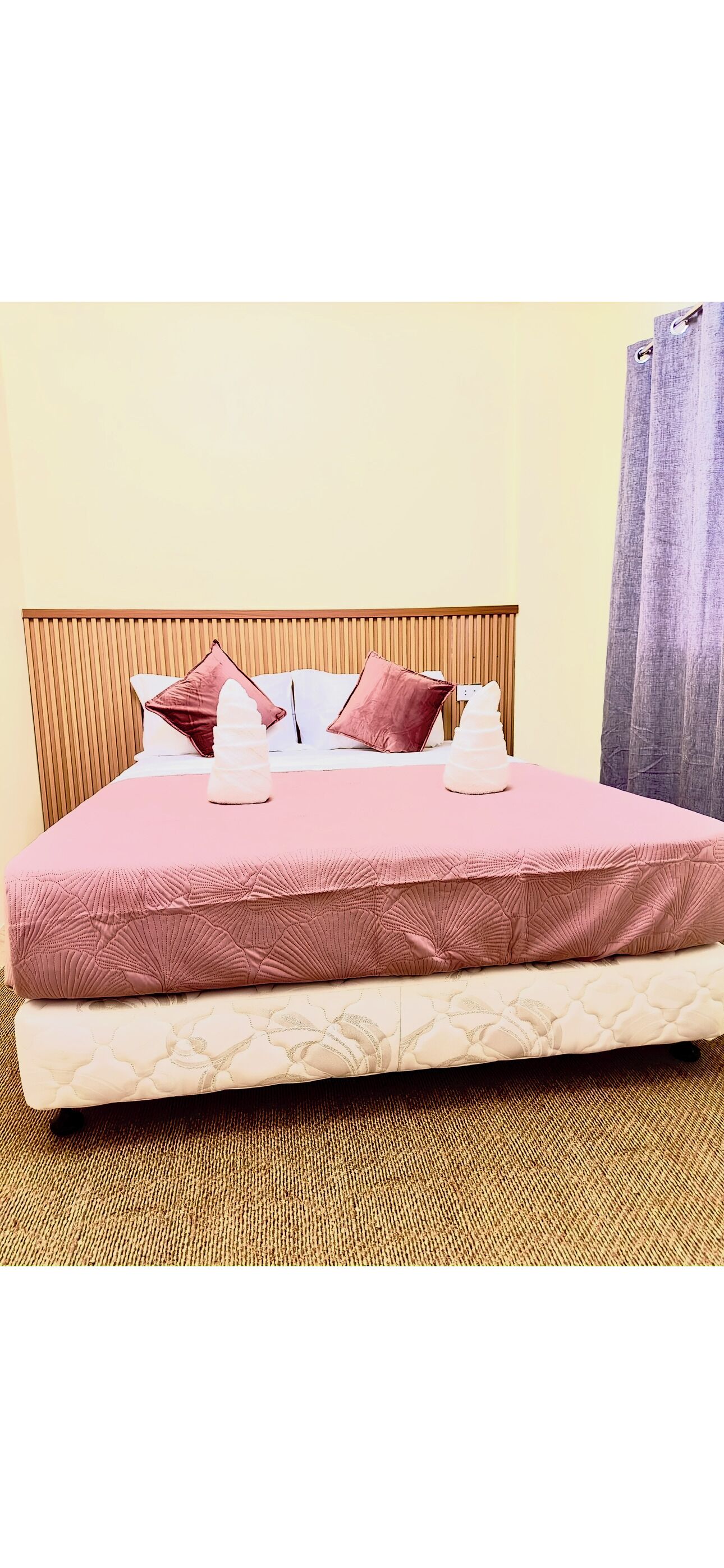 Un lit avec une tête de lit en bois, une literie rose et un matelas blanc texturé.