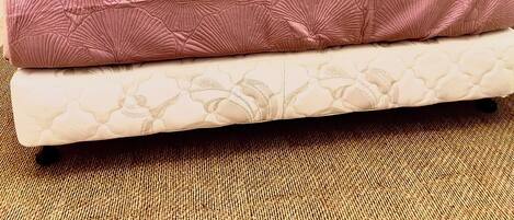 Una cama con cabecera de madera, ropa de cama rosa y colchón blanco con textura.