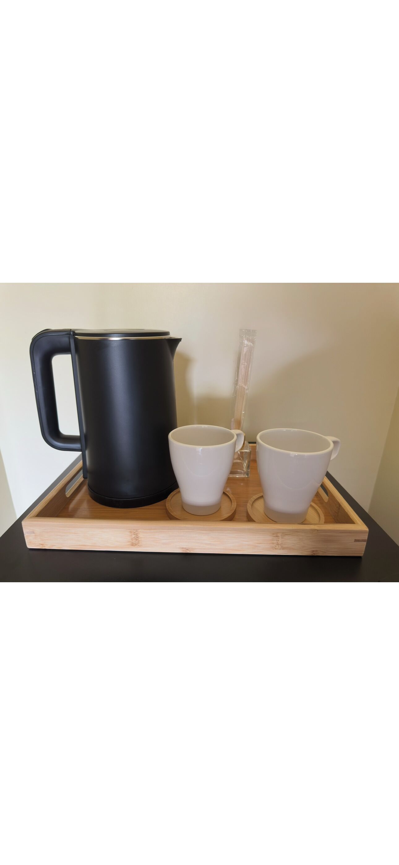 A black kettle, two white cups, and a glass on a wooden tray.