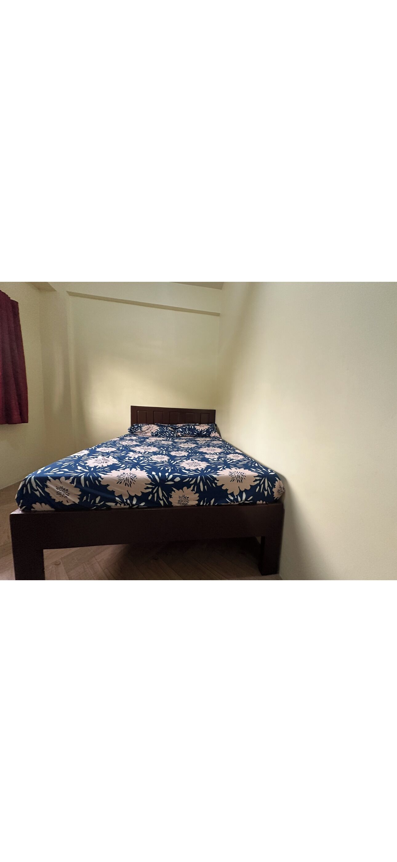 Una cama con colcha estampada en una habitación con pared lisa y suelo de madera.