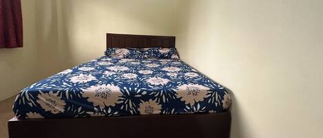 Una cama con colcha estampada en una habitación con pared lisa y suelo de madera.