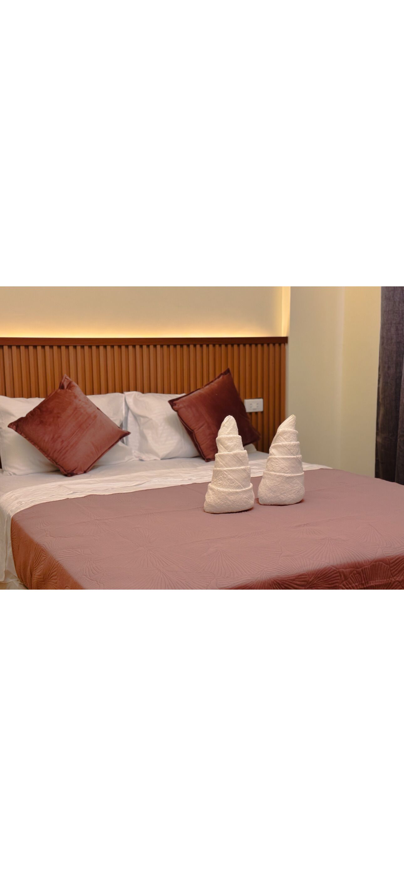 A bed with a wooden headboard, white and brown pillows, and a pink bedspread.