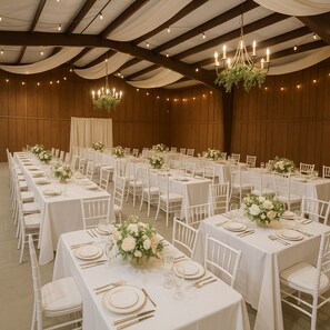 A banquet hall with long tables, white chairs, chandeliers, and floral centerpieces. - Zebra Ranch 150 Guest Venue Lodging Mtn Vu Farm (Prescott)