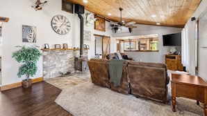 Una sala de estar acogedora con un sofá marrón, una chimenea, un reloj y un ventilador de techo.
