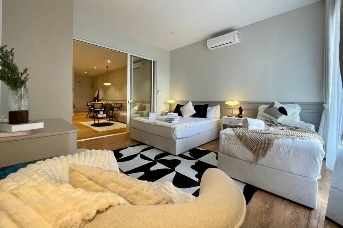 Habitación de hotel moderna con una cama grande, un sofá, un escritorio y un área de comedor visible a través de una puerta de cristal.