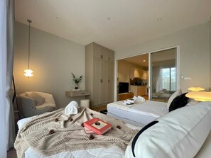 A modern hotel room with a bed, a sofa, a desk, and a large sliding door leading to a kitchen area. - Quill Residences By Happy Stay (Kuala Lumpur)
