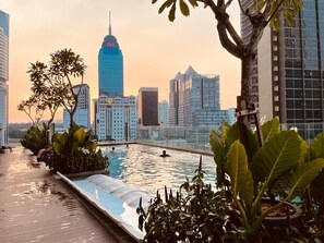 Una piscina en la azotea con un horizonte urbano al fondo, rodeada de follaje.