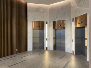 Un área de ascensor moderna con paredes de mármol, paneles de madera e indicadores digitales de pisos.