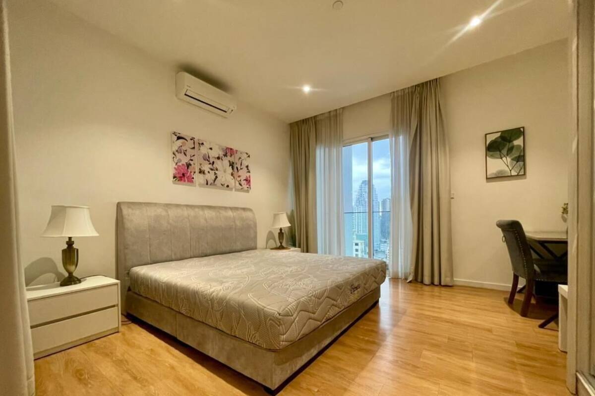 Habitación de hotel con una cama grande, mesitas de noche con lámparas, un escritorio y vistas a la ciudad.