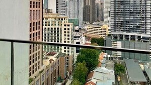 Paisagem urbana com edifícios altos, um arranha-céu imponente e vista para uma rua com carros estacionados e vegetação.
