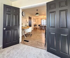 Puerta abierta que da a una habitación con un escritorio, una silla y un reloj en la pared.