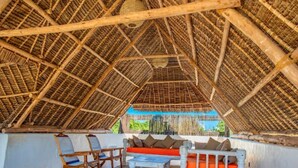 A thatched-roof structure with wooden furniture and a view of the sea.
