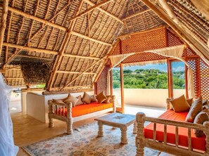 Una habitación con techo de paja, un banco de madera, un sofá y vistas al verdor exterior.