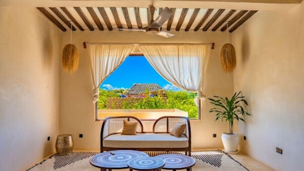 A room with a bed, a table, a potted plant, and a window with a view.