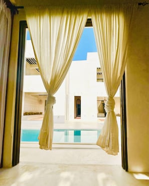 Une chambre avec vue sur une piscine, des rideaux et un bâtiment blanc en arrière-plan.