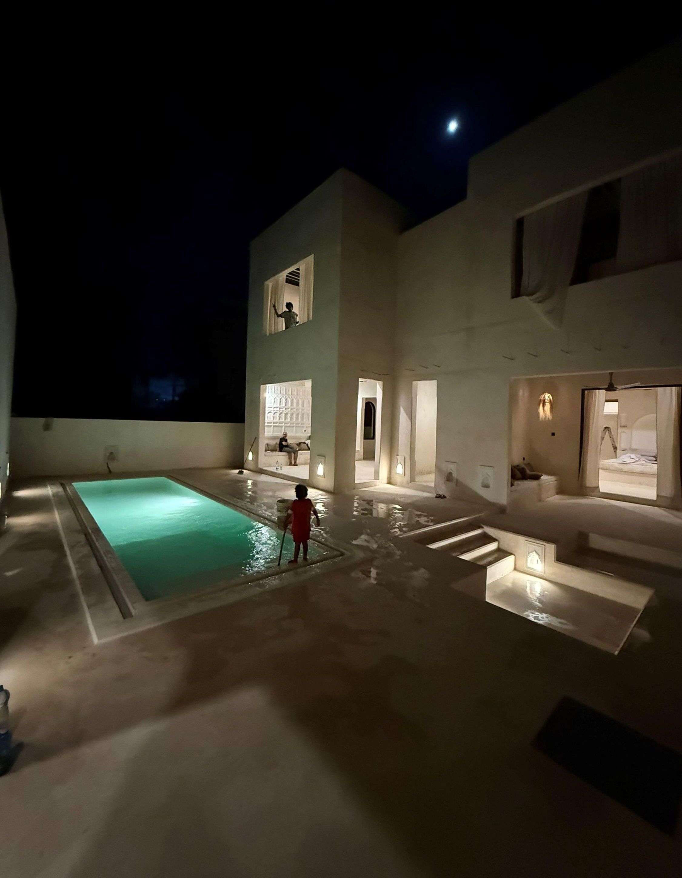 A modern building with a swimming pool, a child playing near the pool, and a person standing on a balcony.