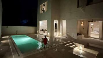 A modern building with a swimming pool, a child playing near the pool, and a person standing on a balcony.