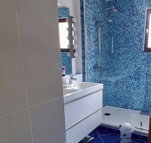 Un baño con un lavabo blanco, un espejo con iluminación, una ducha y mosaicos azules.