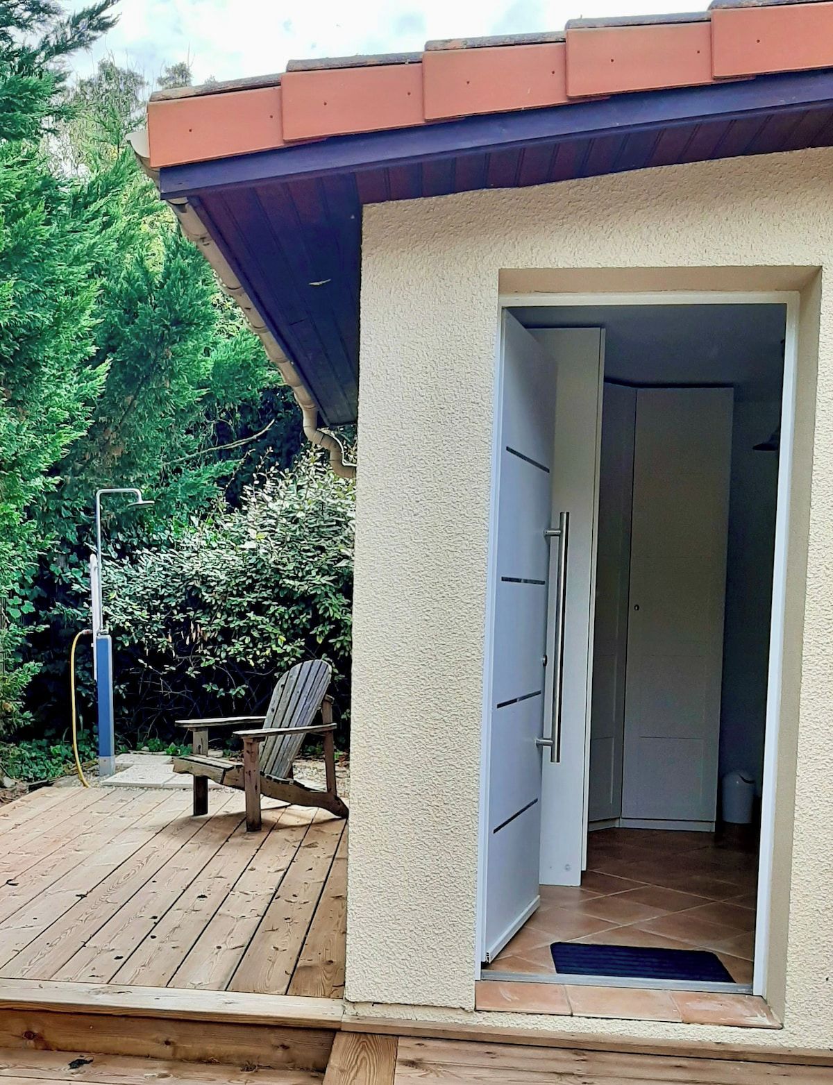 A wooden deck with a chair, a door leading to a room, and a covered area with a red roof.