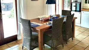En matplats med flätade stolar, ett träbord, en hängande lampa och ett kök med vitvaror.