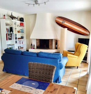 Una sala de estar con chimenea, una estantería, un sofá, un sillón amarillo y una decoración con una tabla de surf.