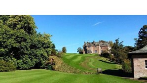 Ein Golfplatz mit Clubhaus und einer großen Baum.