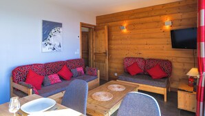 A cozy room with a wooden wall, a television mounted above a sofa, and a dining table with chairs. - Chalet apartment for rent with south-facing terrace and private sauna (saint francois longchamp)