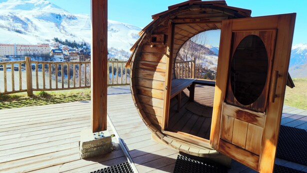A wooden cabin with a curved exterior, a bench inside, and a view of snow-capped mountains. - Chalet apartment for rent with south-facing terrace and private sauna (saint francois longchamp)