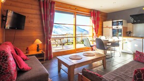 A cozy room with a sofa, a table, and a view of mountains through large windows. - Chalet apartment for rent with south-facing terrace and private sauna (saint francois longchamp)