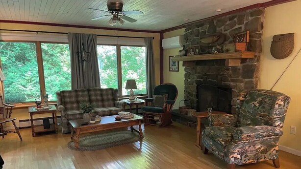 Una sala de estar con chimenea de piedra, un sofá a cuadros, un sillón verde y una mesa de centro de madera.