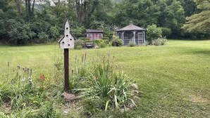 Un espacio verde con un comedero para pájaros, un pabellón y un pequeño edificio con porche.