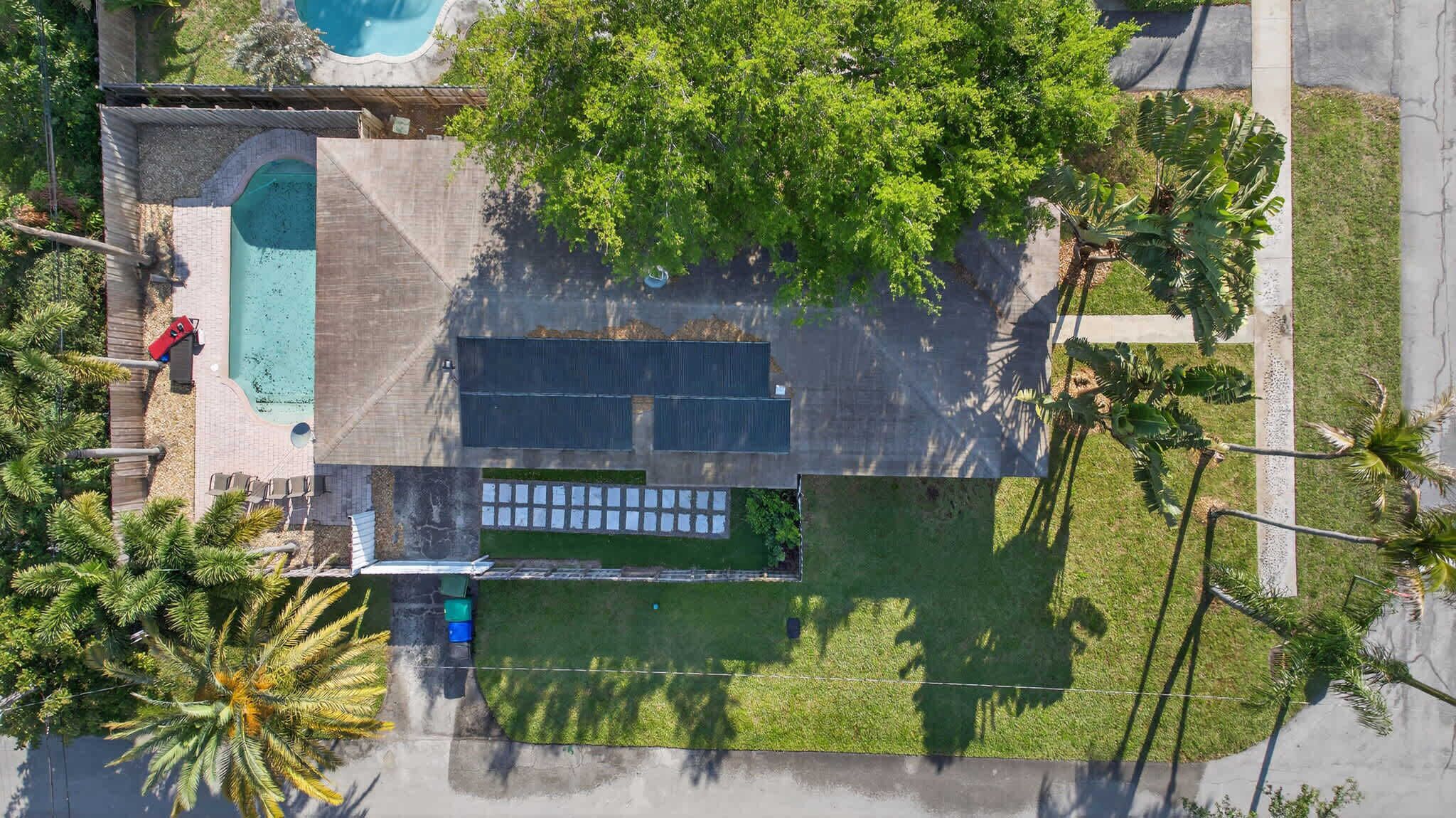 Vista aérea de uma propriedade com piscina, alpendre coberto e um extenso gramado verde.
