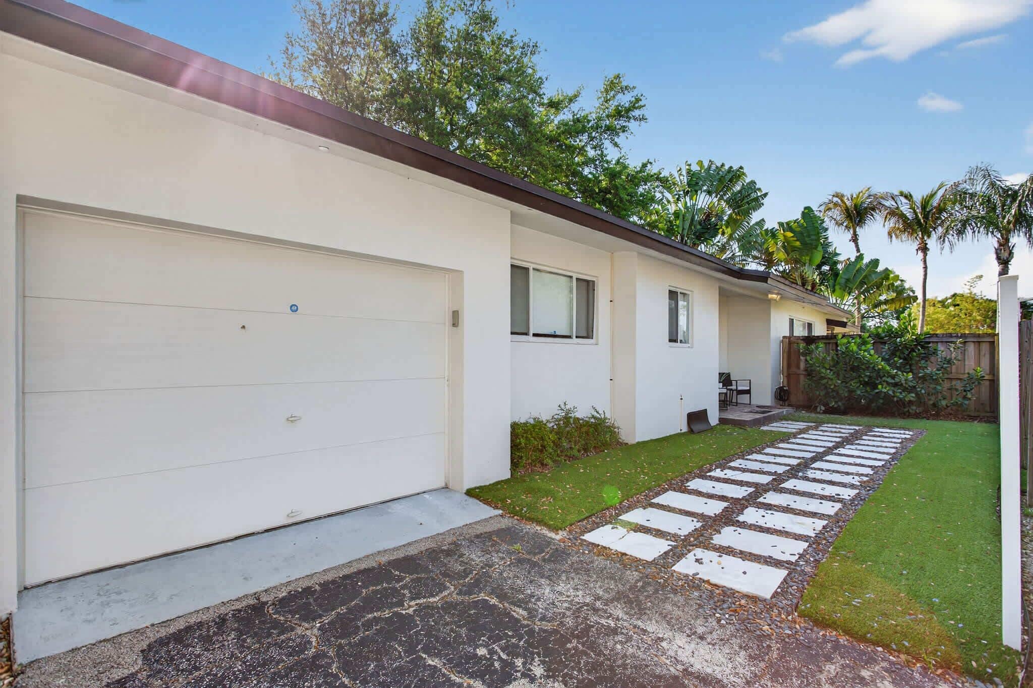 A residential building with a garage, a small porch, and a paved walkway leading to the entrance.