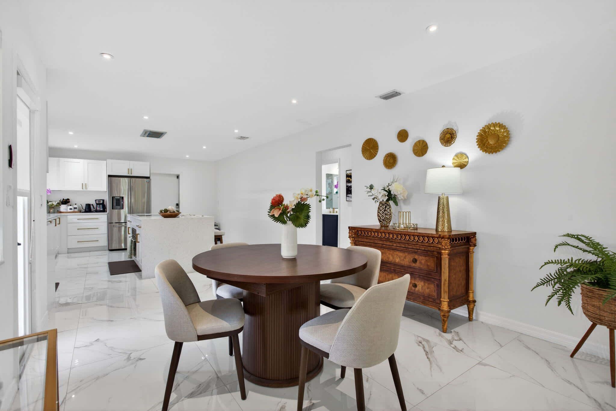 A modern kitchen with white cabinets, a stainless steel refrigerator, and a dining area with a round wooden table and chairs.