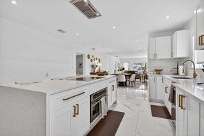 A modern kitchen with white cabinetry, a central island, and a dining area in the background. - Tropical Oasis w/ Private Pool (Fort Lauderdale)