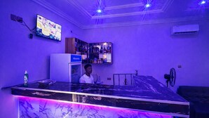 A bar area with a marble countertop, a refrigerator, and a television mounted on the wall. - The Whale Inn (Kaduna)